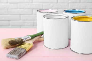 Photo of Cans of colorful paints and brushes on pink table