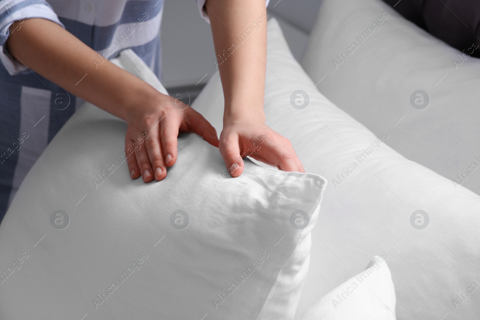 Photo of Woman fluffing white pillow on bed, closeup