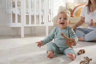 Cute baby girl playing with wooden toys and mother on floor at home