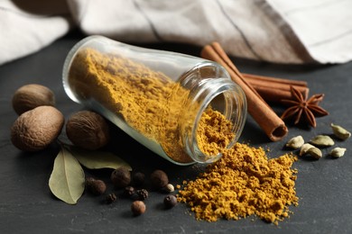 Photo of Jar with dry curry powder and other spices on dark textured table, closeup