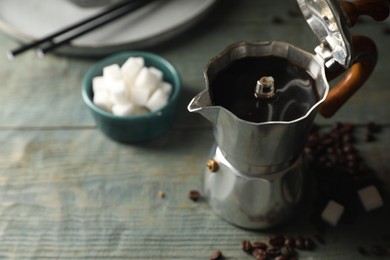 Brewed coffee in moka pot, beans and sugar cubes on rustic wooden table, closeup. Space for text