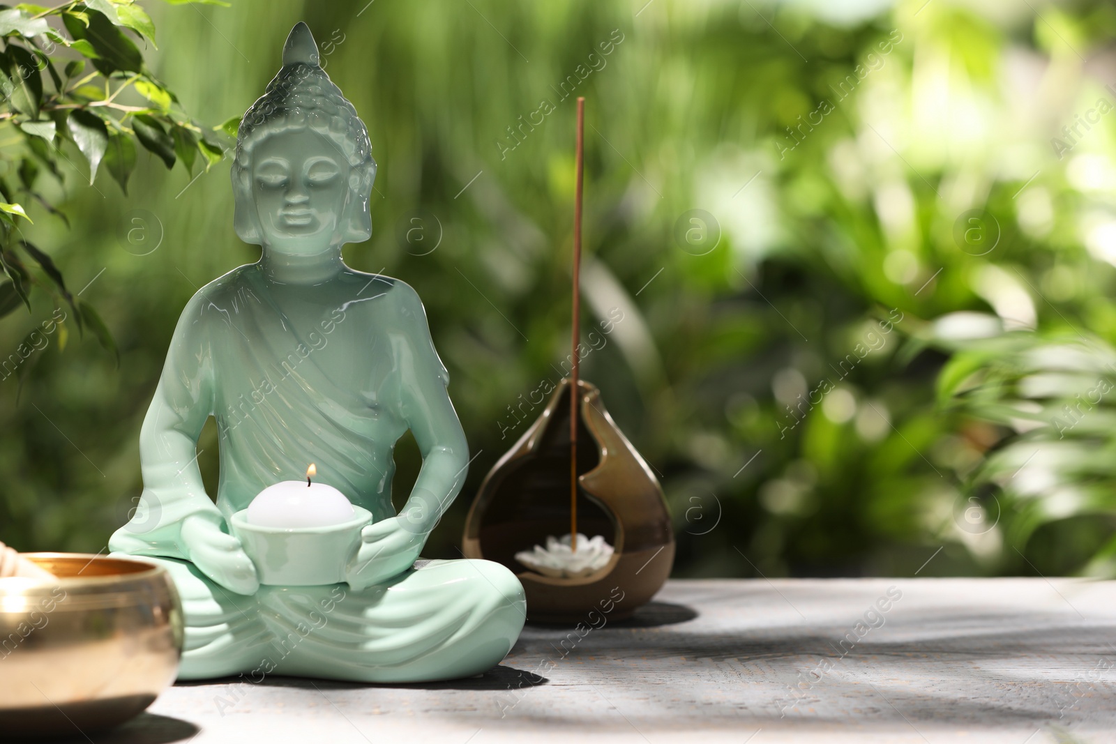 Photo of Buddhism religion. Decorative Buddha statue with burning candle on wooden table outdoors, space for text