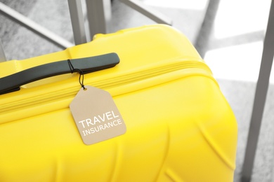 Photo of Yellow suitcase with TRAVEL INSURANCE label at stairs indoors, closeup