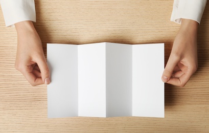 Photo of Woman holding blank brochure mock up on wooden table, top view