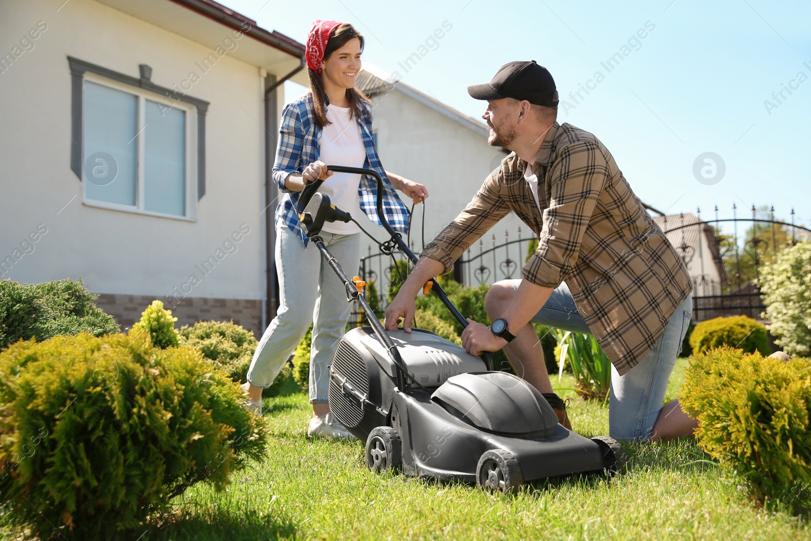 Photo of Happy couple spending time together while cutting green grass with lawn mower in garden