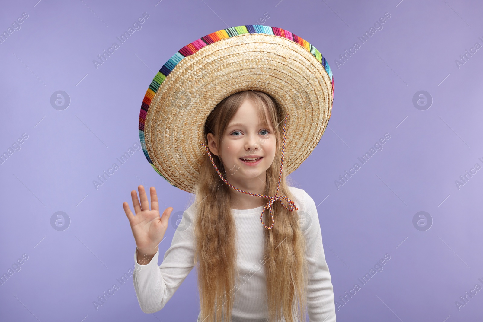 Photo of Cute girl in Mexican sombrero hat waving hello on purple background