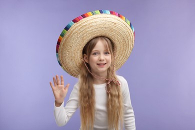 Cute girl in Mexican sombrero hat waving hello on purple background