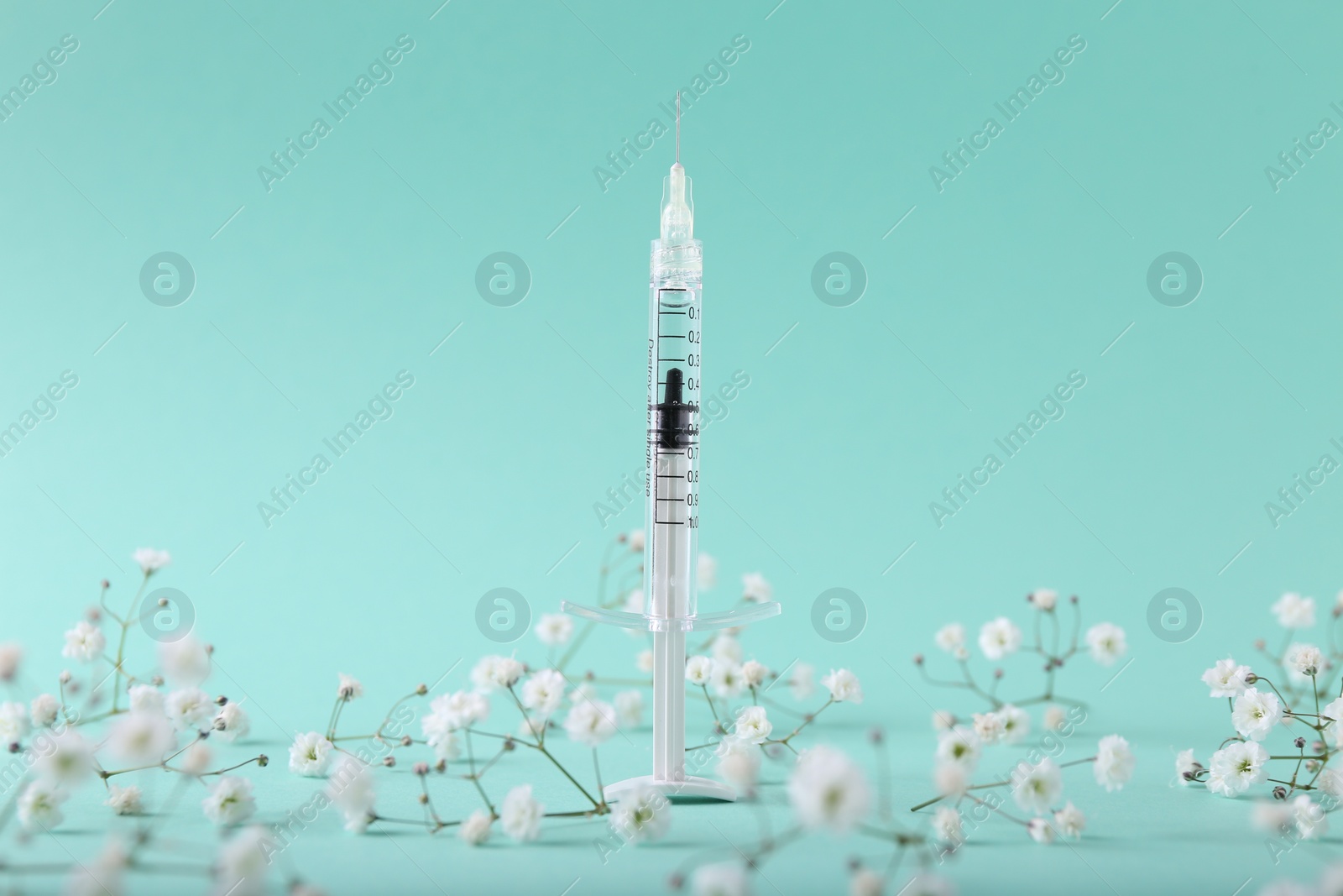 Photo of Cosmetology. Medical syringe and gypsophila flowers on turquoise background