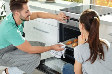 Photo of Young couple baking croissants in oven at home