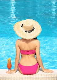 Photo of Young woman with cocktail sitting near swimming pool