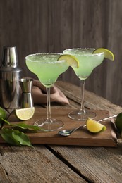 Photo of Delicious Margarita cocktail in glasses, limes and bartender equipment on wooden table