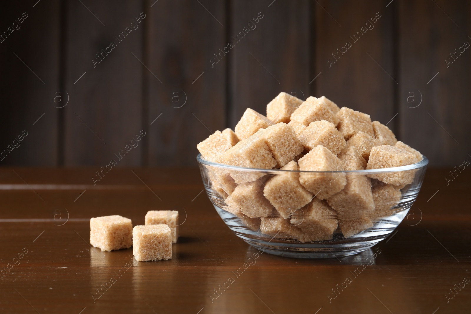 Photo of Brown sugar cubes in glass bowl on wooden table