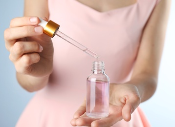 Photo of Young woman dripping rose essential oil into glass bottle, closeup