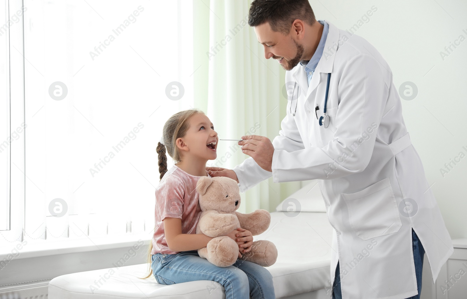 Photo of Children's doctor examining little patient's throat in clinic