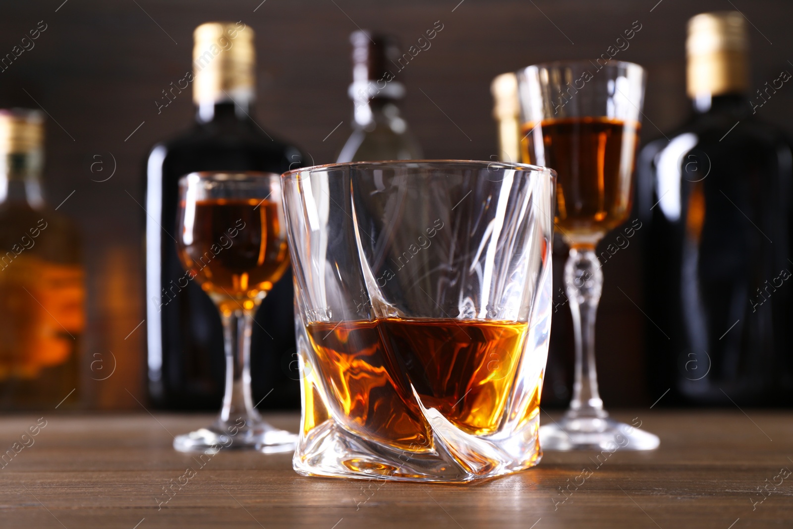 Photo of Different delicious liqueurs in glasses and bottles on wooden table, closeup