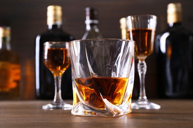 Different delicious liqueurs in glasses and bottles on wooden table, closeup