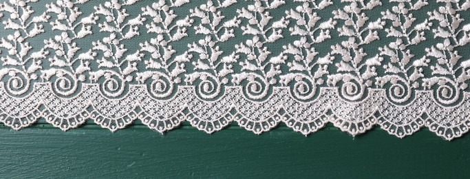 Photo of Beige lace on green wooden table, top view