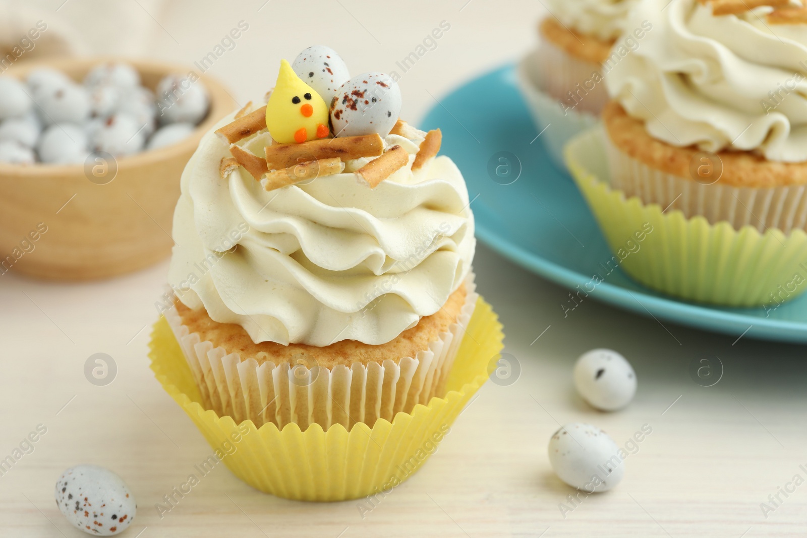 Photo of Tasty Easter cupcakes with vanilla cream on light wooden table, closeup