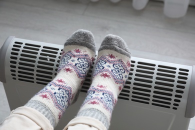 Photo of Woman warming feet on electric heater at home, closeup