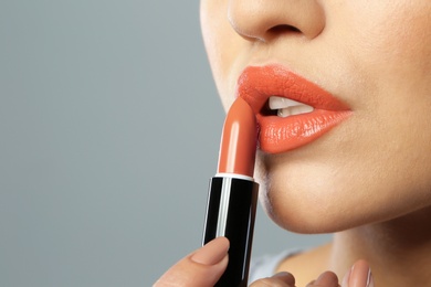 Photo of Young woman applying beautiful lipstick on gray background, closeup. Space for text