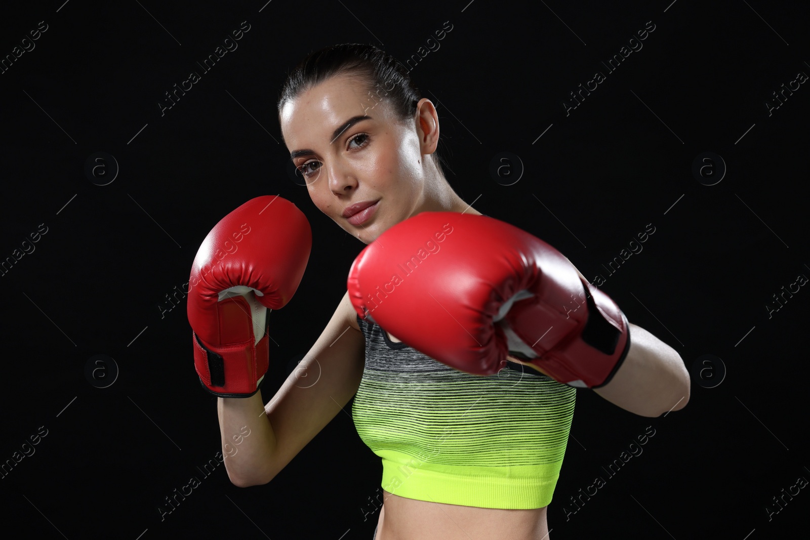 Photo of Beautiful woman in boxing gloves training on black background