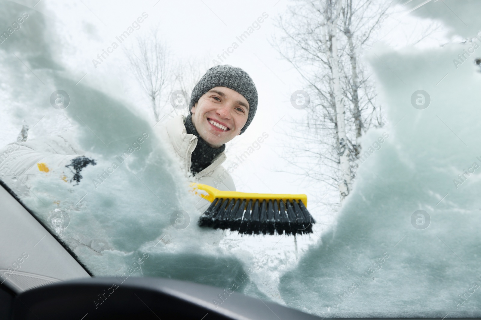 Photo of Man cleaning snow from car windshield, view from inside