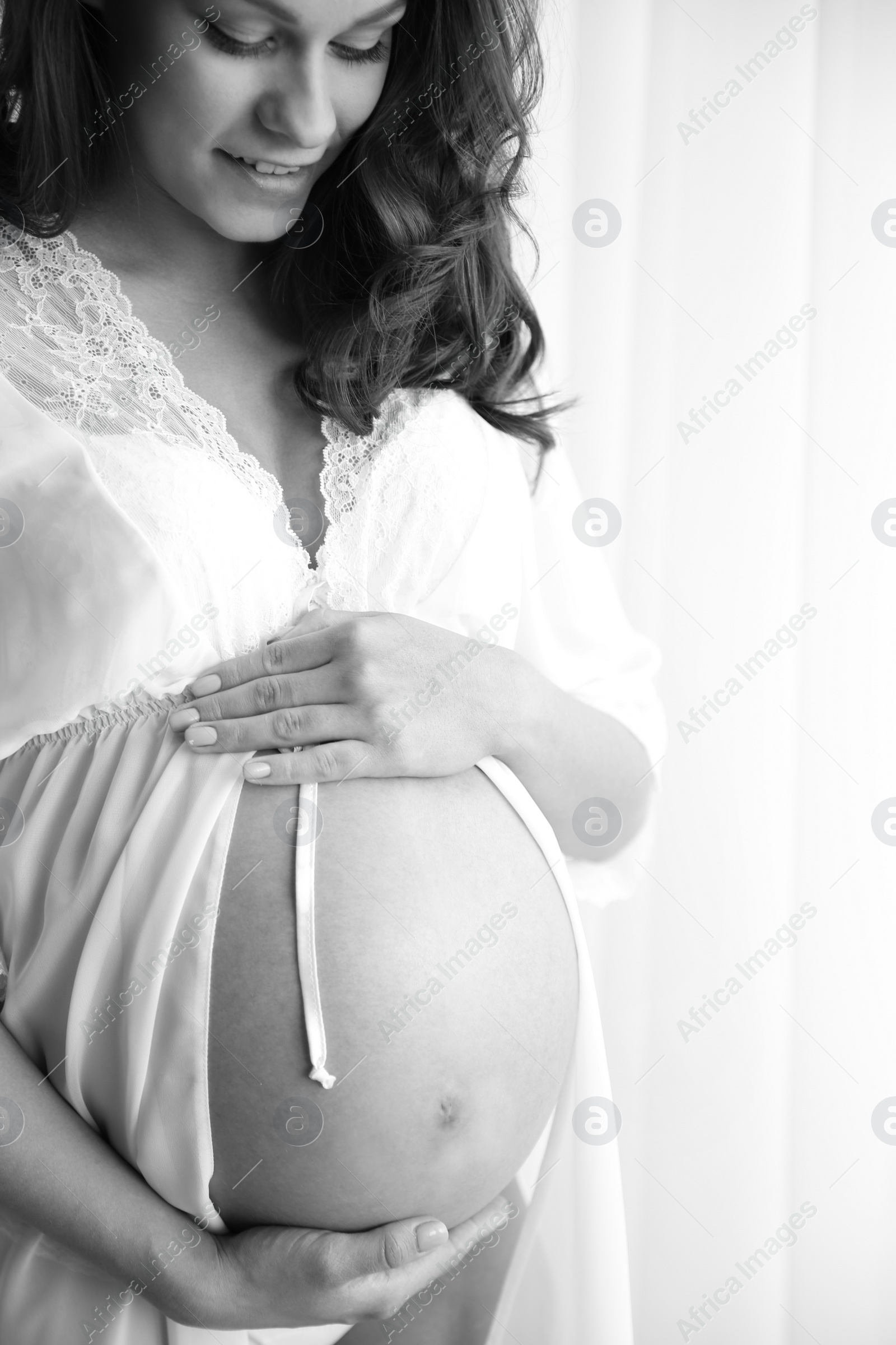 Photo of Young pregnant woman in lace nightgown on light background, black and white effect