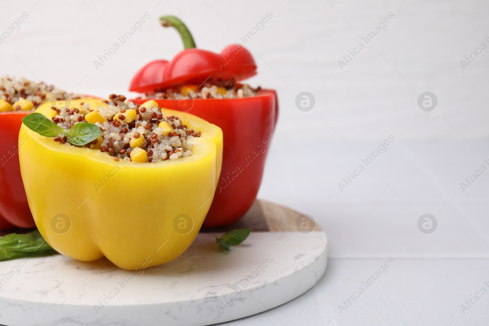 Photo of Quinoa stuffed bell peppers and basil on white table, closeup. Space for text