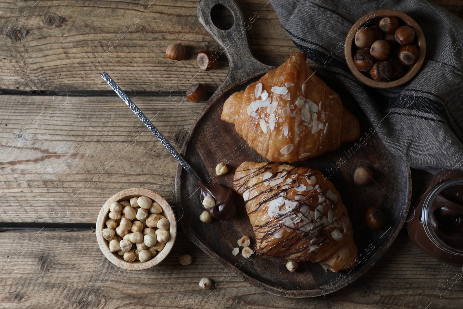 Photo of Delicious croissants with chocolate and nuts on wooden table, flat lay