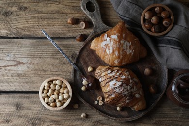 Photo of Delicious croissants with chocolate and nuts on wooden table, flat lay