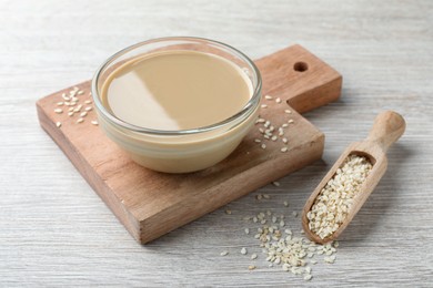 Photo of Tasty sesame paste and seeds on white wooden table
