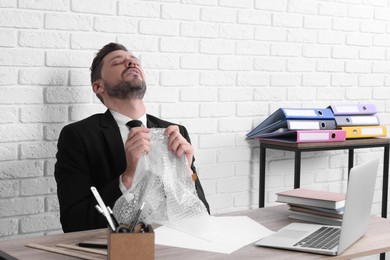 Businessman popping bubble wrap at workplace in office. Stress relief