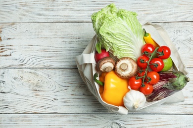 Bag full of fresh vegetables on wooden background, top view. Space for text