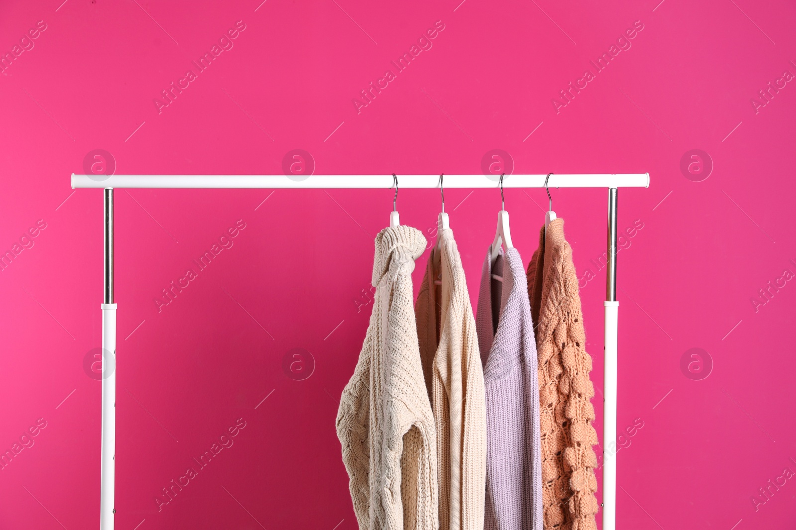 Photo of Collection of warm sweaters hanging on rack against color background