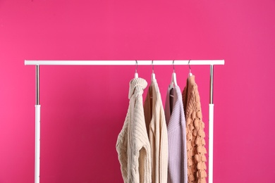 Photo of Collection of warm sweaters hanging on rack against color background