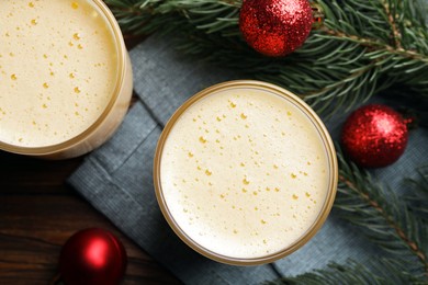Photo of Glasses of delicious eggnog and decorated fir branch on wooden table, flat lay