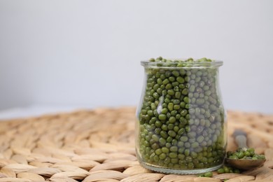 Photo of Glass jar of mung beans with spoon on wicker mat against white background, closeup. Space for text