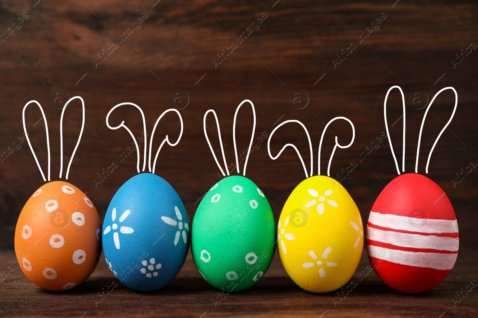 Image of Bright Easter eggs with cute bunny ears on wooden background