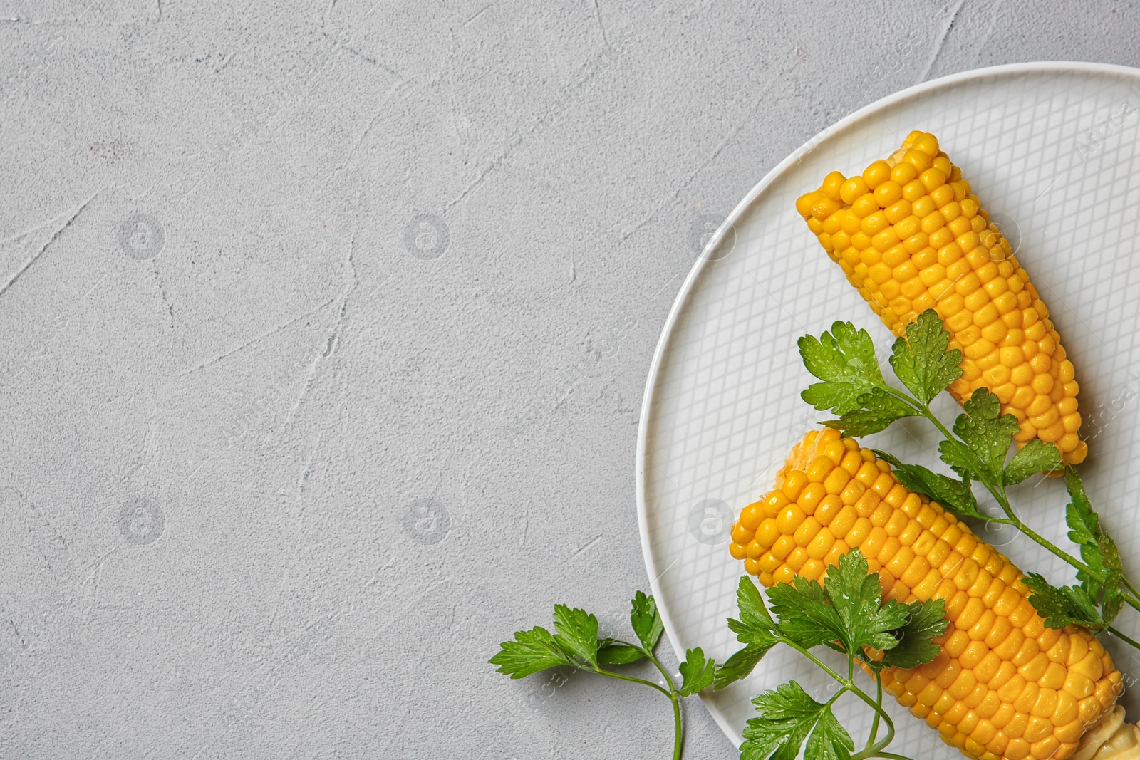 Photo of Plate with ripe corn cobs and parsley on grey background, top view. Space for text