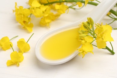 Photo of Rapeseed oil in gravy boat and beautiful yellow flowers on white wooden table, closeup