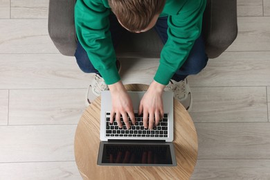 Man working with laptop at wooden table, top view. Space for text