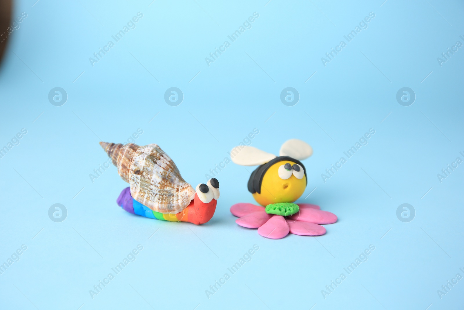 Photo of Beautiful plasticine bee with flower and snail on light blue background. Children's handmade ideas