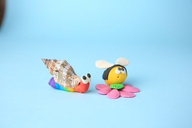 Photo of Beautiful plasticine bee with flower and snail on light blue background. Children's handmade ideas