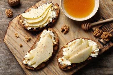 Photo of Toasted bread with tasty cream cheese and pear on wooden table, flat lay