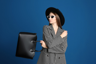 Beautiful young woman in sunglasses with stylish bag on blue background