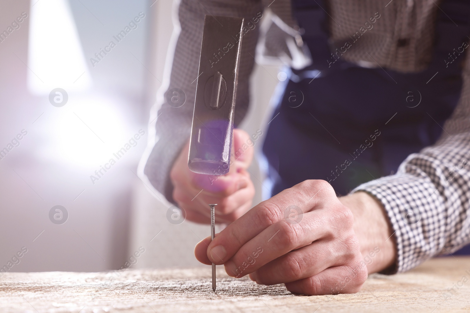 Photo of Professional repairman hammering nail into wooden board indoors, closeup