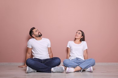 Young couple sitting on floor near pink wall indoors