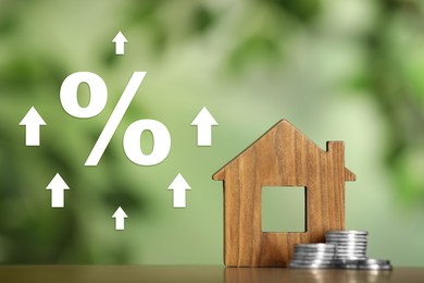Image of Mortgage. Wooden house model, coins, arrows and percent sign on blurred green background