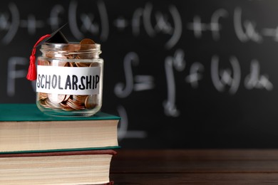 Photo of Scholarship concept. Glass jar with coins, graduation cap and books on wooden table, space for text