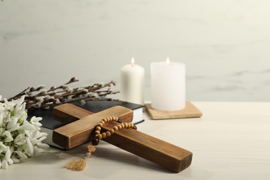 Photo of Burning church candles, rosary beads, wooden cross, Bible, willow branches and snowdrops on white table. Space for text